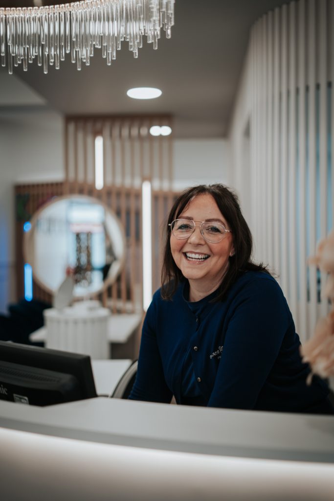 Staff member at Edwards & Walker Opticians Doncaster smiling from behind reception desk.