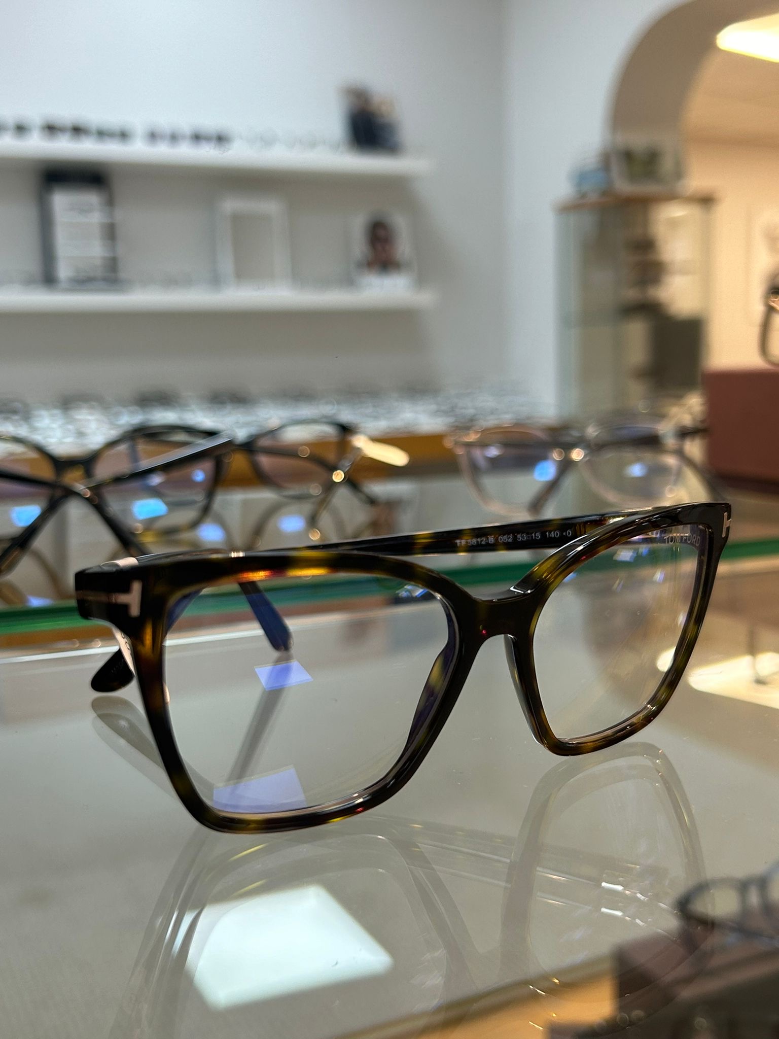 Tortoiseshell Tom Ford eyeglasses with T-bar detailing displayed on a glass counter in a well-lit optician’s showroom.