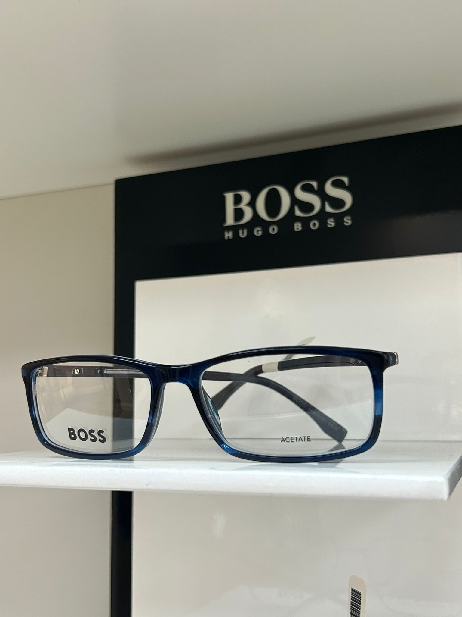 Rectangular blue BOSS Hugo Boss eyeglasses displayed on a white shelf with a branded BOSS sign in the background.