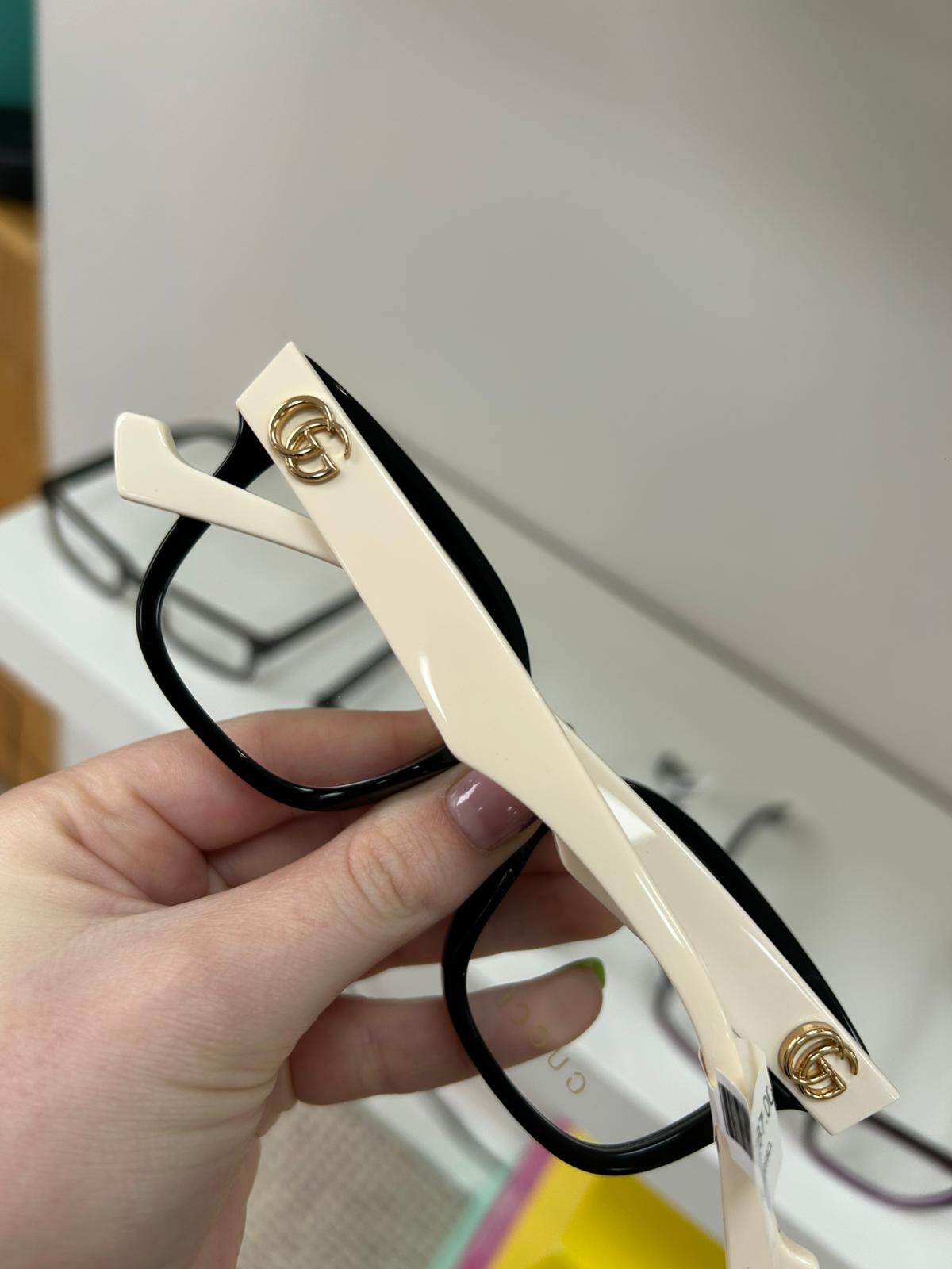Close-up of a Gucci glasses frame with black fronts and ivory temples, detailed with gold GG logo branding.