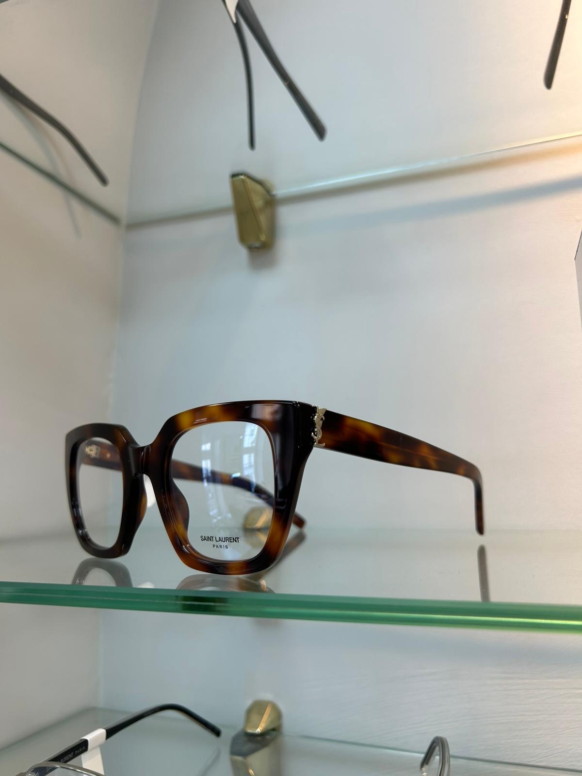 Saint Laurent oversized square Havana tortoiseshell glasses displayed on a glass shelf.