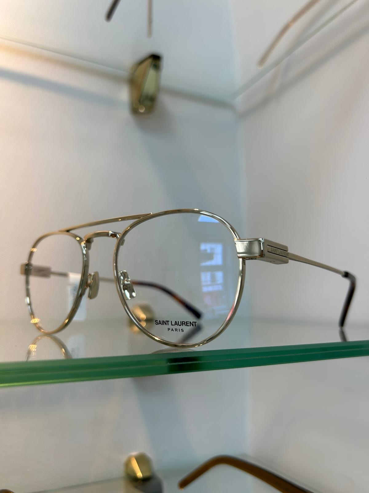 Saint Laurent silver metal aviator glasses with double bridge, displayed on a glass shelf against a white background.