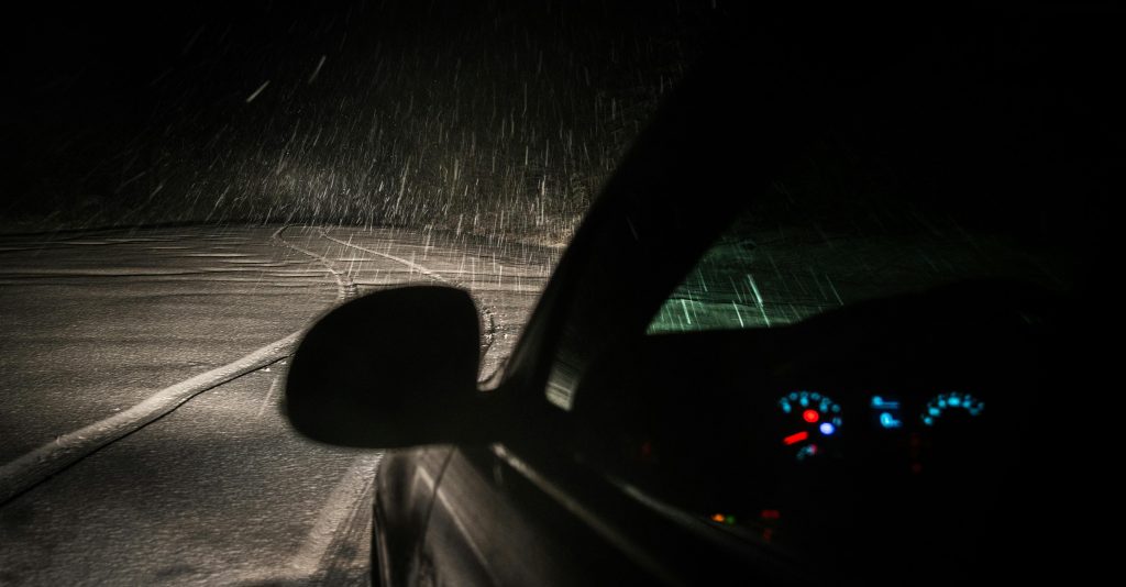 Car on road with headlights on, at night time in the rain