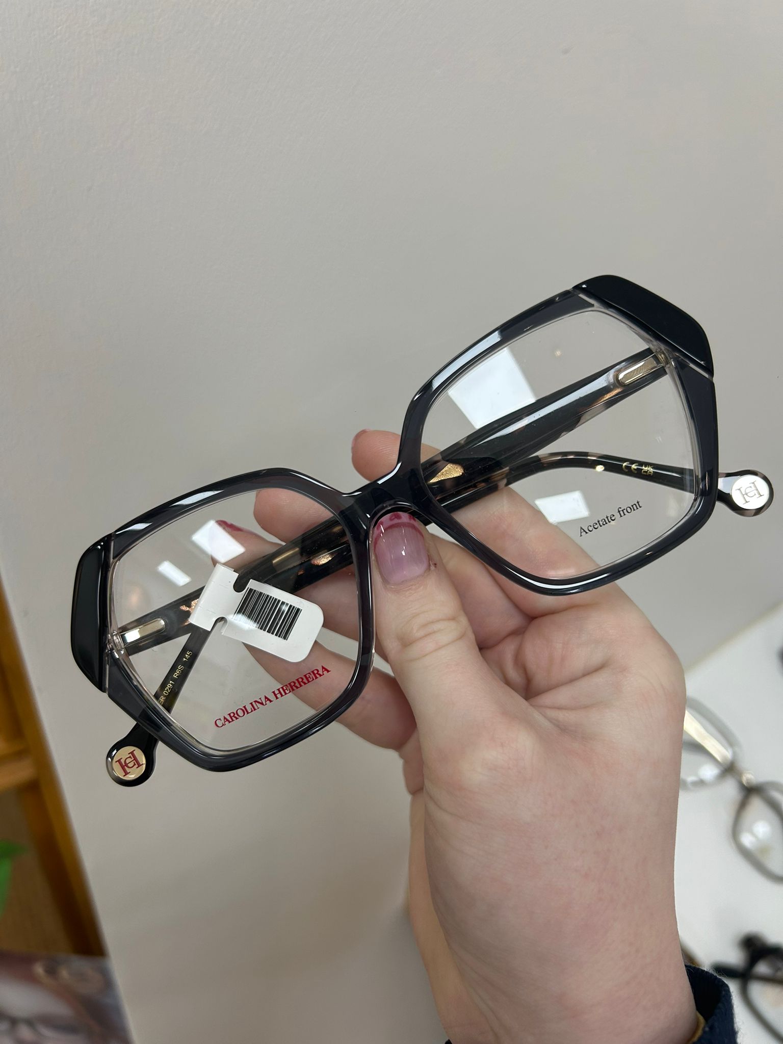 Oversized Carolina Herrera black and clear acetate glasses held in hand, showing red branding and gold CH detail on the temple tips.
