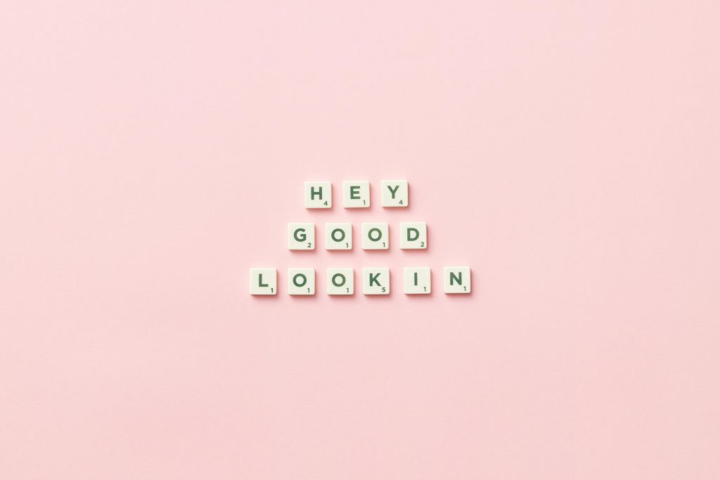 Small white tiles that spell Hey Good Looking on a plain pink background