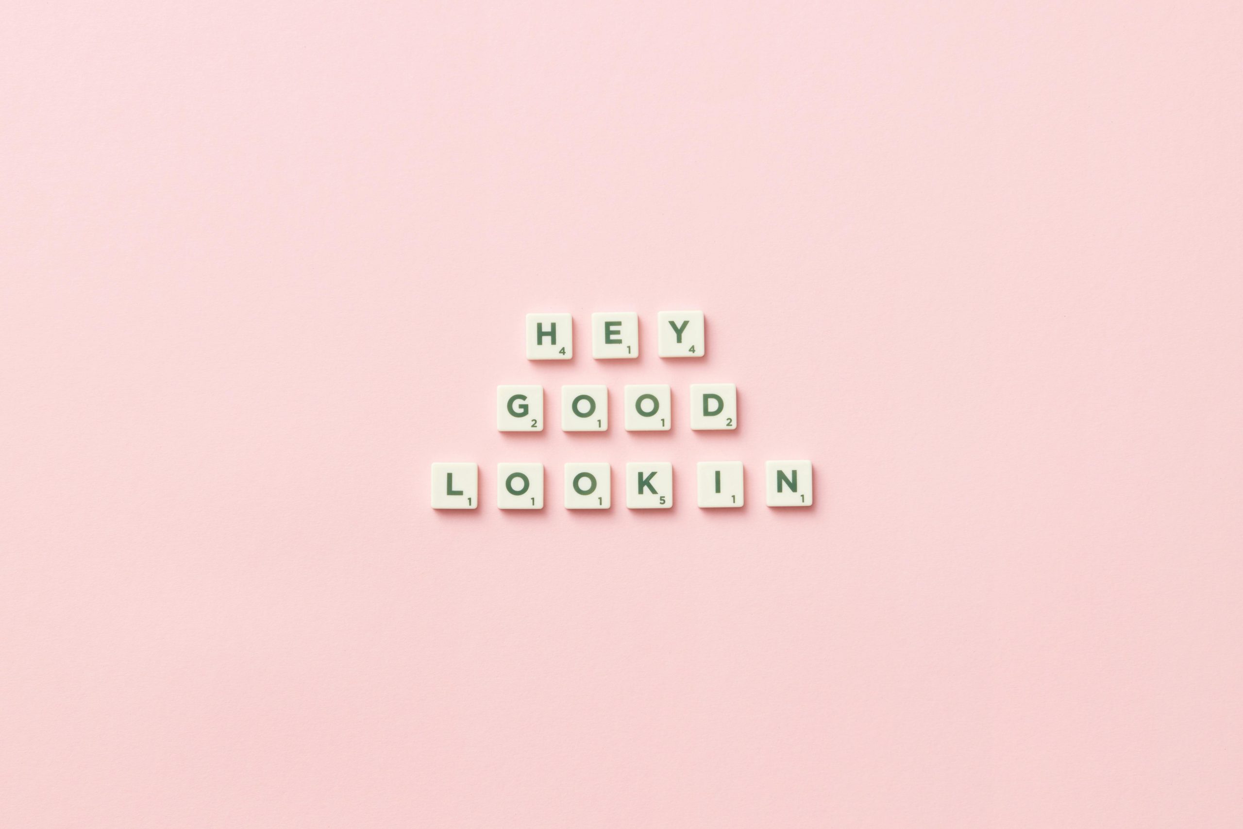 Small white tiles that spell Hey Good Looking on a plain pink background
