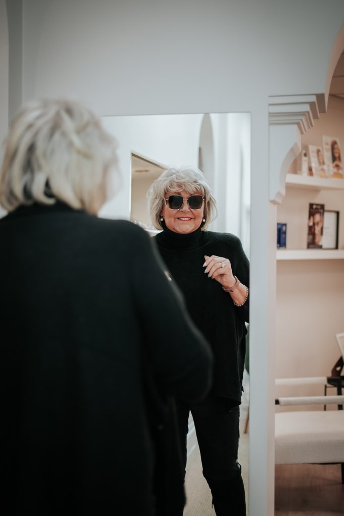 Customer trying on designer sunglasses during an glasses styling consultation at Edwards & Walker Opticians Doncaster, smiling as they view their reflection in a full-length mirror.